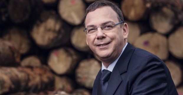 Michael Pfeifer in Anzug und Brille vor einem Holzstoß