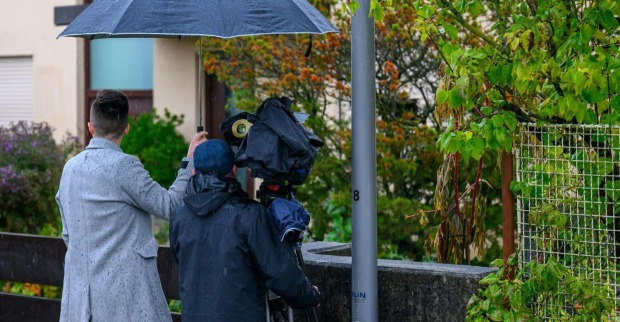 Journalistenteam mit Kamera und Regenschirm dokumentiert den Tatort in Enns nach dem mutmaßlichen Doppelmord.