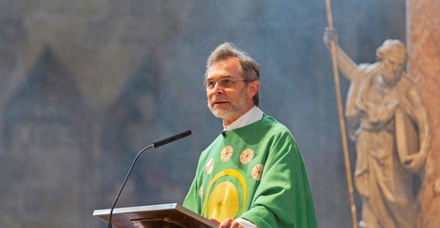 Josef Grünwidl in grüner liturgischer Kleidung predigt am Ambo, hinter ihm steht eine Statue mit Stab.