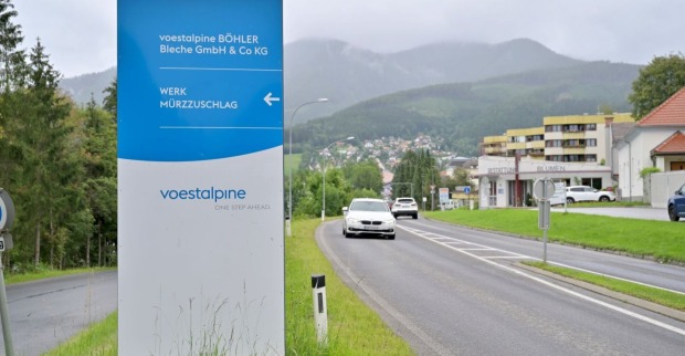 Einfahrtsschild des Voestalpine-Werks Böhler Bleche in Mürzzuschlag mit Blick auf die Straße und die umliegende Stadt im Hintergrund.