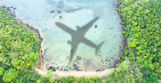 Luftaufnahme einer Küste mit grünem Wald und türkisfarbenem Wasser, in dem der Schatten eines Flugzeugs zu sehen ist. Symbolfoto für die Einstellung des Flugbetriebs der Regionalfluglinie Blue Islands.