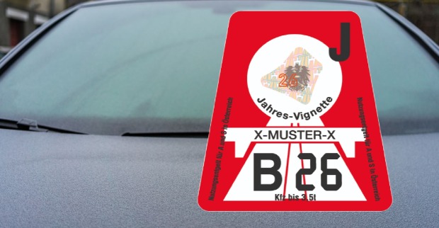 Rote österreichische Jahresvignette 2026 mit der Aufschrift „Jahres-Vignette“ und Kennzeichenfeld, angebracht an einer Autoscheibe.