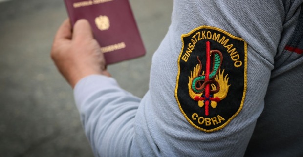 Beamter des Einsatzpolizeikommandos Cobra in Uniform und einem österreichischen Reisepass in seiner Hand
