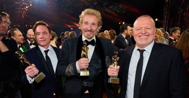 Thomas Gottschalk hält bei der Kurier Romy 2025 in Kitzbühel seine Diamant-Romy in den Händen, flankiert von den zwei weiteren Sonderpreisträgern Bully Herbig und Stefan Raab, umgeben von Gästen in festlicher Abendgarderobe.