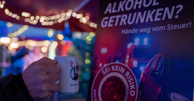 Hand die einen Punschbecher hält. Im Hintergrund ein Plakat der Aktion GEMEINSAM SICHER