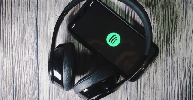 Kopfhörer auf einer grauen Holzoberfläche um ein iPhone auf dem das App-Icon von Spotify angezeigt wird