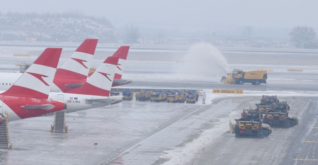 Winterdienstfahrzeuge räumen vereiste Pisten am Flughafen Wien-Schwechat, mehrere Austrian-Airlines-Flugzeuge stehen still; deutliche Auswirkungen des Glatteischaos auf den Flugbetrieb.