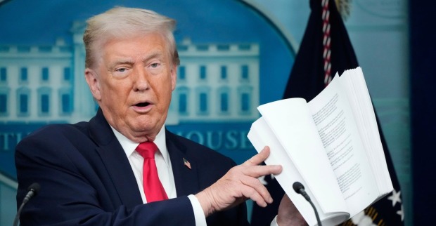 Donald Trump hält ein aufgeschlagenes Dokument in den Händen und erklärt die Inhalte seines geplanten internationalen Friedensrats im Weißen Haus.
