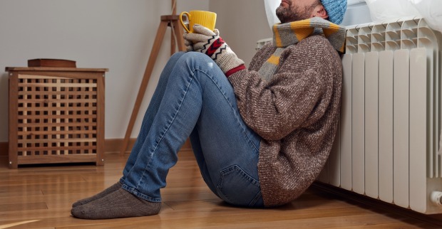 Mann mit Erkältung sitzt mit Tee vor einer Heizung