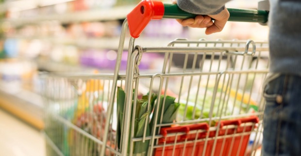 Mann in einem Supermarkt, mit einem gefüllten Einkaufswagen, in welchem sich Lebensmittel befinden