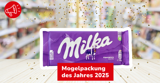 Milka Alpenmilch Schokoladentafel mit dem Hinweis „Mogelpackung des Jahres 2025“ vor einem unscharfen Supermarktregal.
