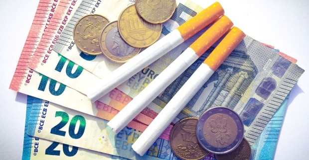 Zigaretten liegen auf Euro-Geldscheinen und Münzen – Symbolbild zur Zigaretten-Preiserhöhung in Österreich.