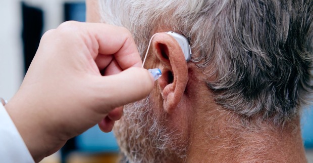 Akustiker steckt Hörgerät in das Ohr eines Mannes mit grauen Haaren
