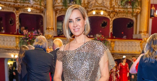 Nadja Bernhard in einem goldfarbenen Abendkleid in einem prunkvollen Theatersaal mit roten Logen im Hintergrund.