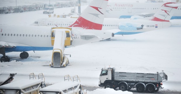 Verschneite Flugzeuge am Flughafen Wien-Schwechat, während Räumfahrzeuge versuchen, die Startbahnen von Schnee zu befreien.