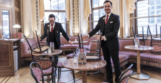 zwei Kellner stellen im Kaffeehaus die Sessel auf den Tisch