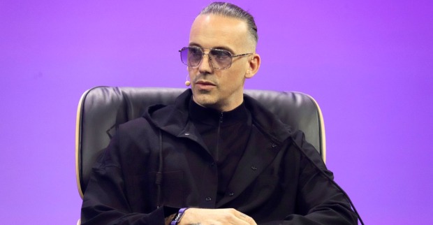 RAF Camora sitzt auf einer Bühne bei einem Interview oder Panel, trägt schwarze Kleidung und eine Sonnenbrille und spricht über seine Rückkehr von Dubai nach Wien nach den Iran-Angriffen.