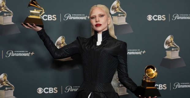 Eine blonde Frau im schwarzen Kleid hält zwei Trophäen hoch