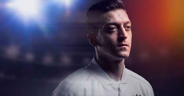 Mesut Özil blickt nachdenklich, im Hintergrund ist ein Stadion zu sehen