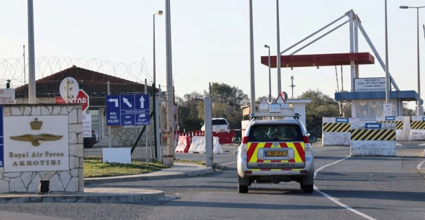 Einfahrt des britischen Royal-Air-Force-Stützpunkts Akrotiri auf Zypern mit Sicherheitsabsperrungen, Warnschildern und einem Einsatzfahrzeug.