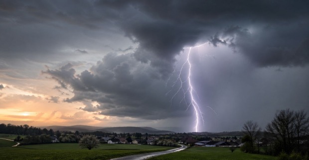 Gewitter in Österreich mit Blitz, dunklen Wolken und Regen über ländlicher Landschaft im Frühling