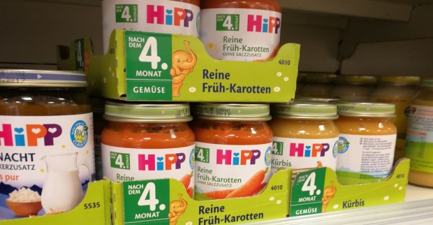 Mehrere Gläser HiPP-Babynahrung der Sorte Karotte und Kürbis stehen dicht gereiht in einem Supermarktregal, während Ermittlungen wegen möglicher Manipulation und Erpressung laufen.