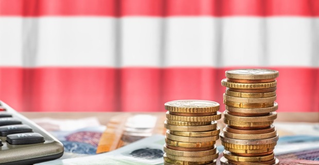 Euro-Münzen und Geldscheine mit Taschenrechner vor Österreich-Flagge symbolisieren Budget Österreich, Sparpaket, Steuern und Pensionen