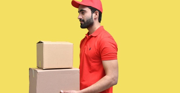 Paketzusteller mit rotem Polo und rotem Kapperl mit zwei Paketen vor einem gelben Hintergrund