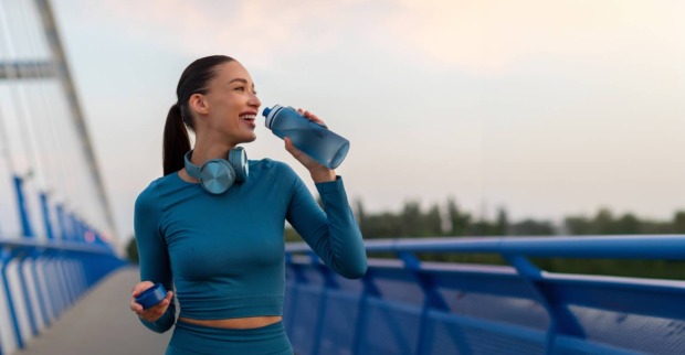 Frau in Sportbekleidung mit Trinkflasche in der Natur