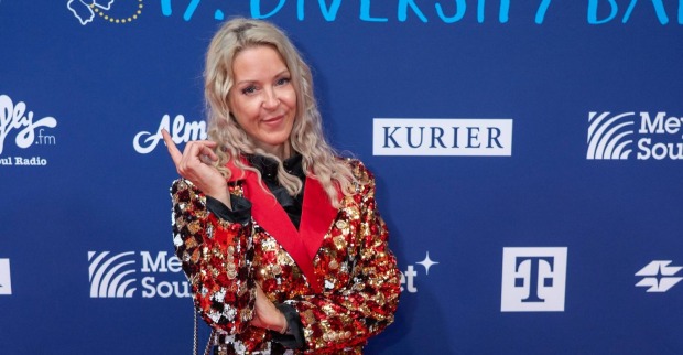 Simone Lugner posiert bei einem Event in einem glitzernden roten Pailletten-Blazer vor einer Sponsorenwand in Wien.
