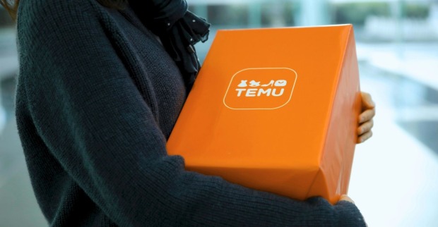 Eine Person im dunkelblauen Pullover trägt ein oranges Temu-Paket
