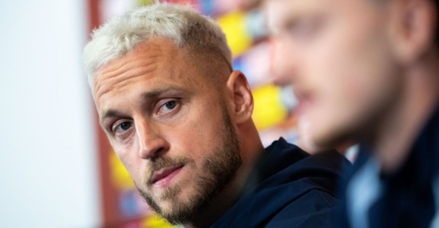 Mann mit blonden Haaren blickt ernst in die Kamera