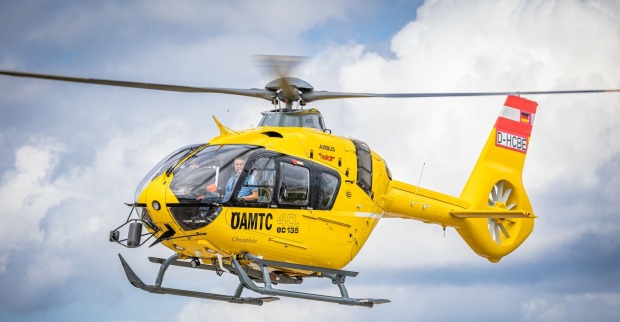 Ein gelber Notarzthubschrauber fliegt vor einer alpinen Bergkulisse