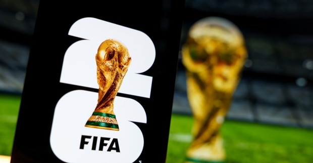 Offizielles FIFA World Cup 2026 Markenlogo auf einem digitalen Bildschirm neben einem unscharfen Trophäenhintergrund.