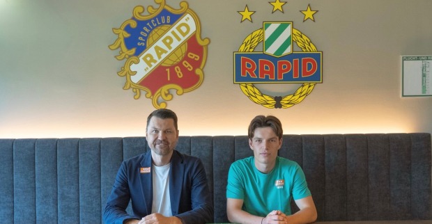 Fußballprofi Nicolas Bajlicz im Shirt des SK Rapid Wien lächelt bei der Vertragsunterzeichnung in der Geschäftsstelle