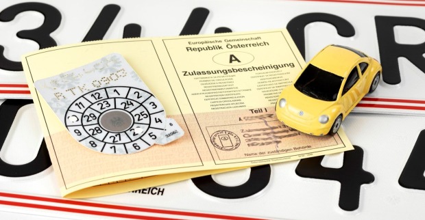 Zulassungsschein, ein Pickerl sowie ein Miniaturauto sind zu sehen