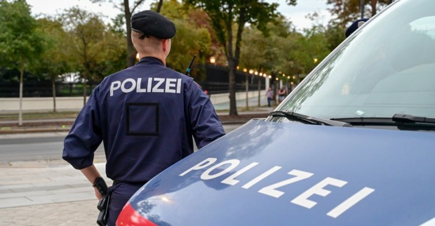 Polizist mit dem Polizeiwagen. Polizist in einheitlicher Patrouille auf der Straße. Polizeisymbol am Fahrzeug und Uniform für die Bluttat in Kärnten.