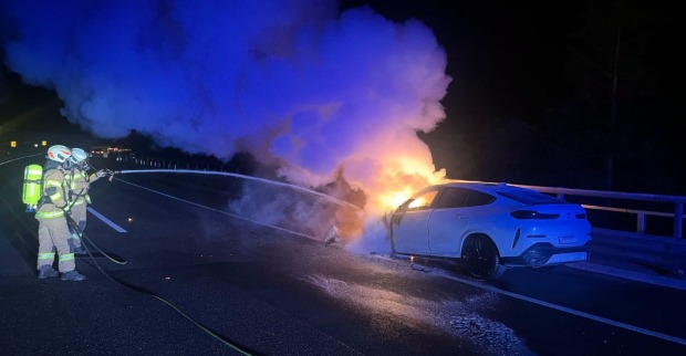 Die Feuerwehr löscht in der Nacht unter Atemschutz ein brennendes Auto auf der Autobahn
