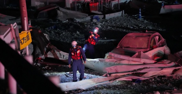 Zerstörte Gebäude und zwei Feuerwehrmänner nach dem Erdbeben in Kumamoto, Japan