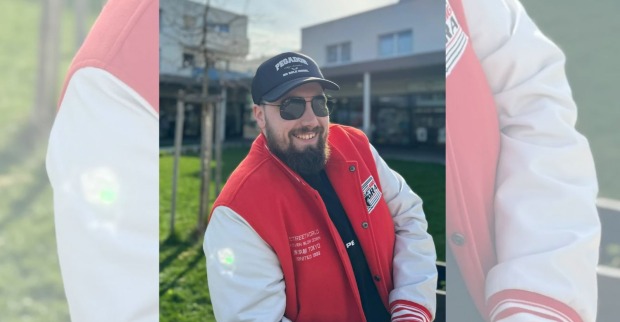 Der Gastro-Influencer Robert erobert steht in einer College-Jacke vor einem Baum
