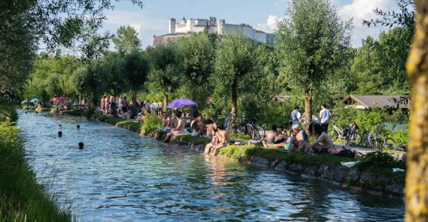 Viele Menschen baden im Almkanal in Salzburg an einem Sommertag, im Hintergrund ist die Festung Hohensalzburg zu sehen; Gülle nach einem Unwetter verursacht Erkrankungen bei Badegästen