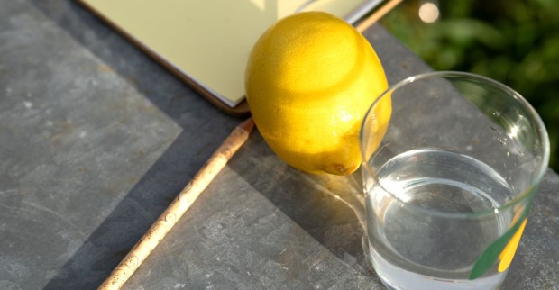 Ein Glas Wasser mit einer Zitrone steht an einem heißen Sommertag auf einem Tisch