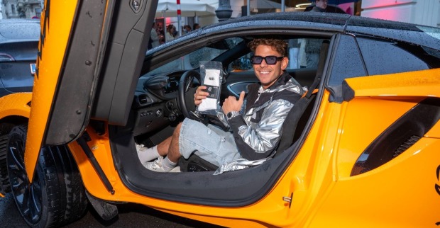 MaxaMillion posiert in einem Sportwagen mit Produkten seiner Marke Gamechangersocks. Der Wiener Influencer verlost drei BMW im Wert von 150.000 Euro.