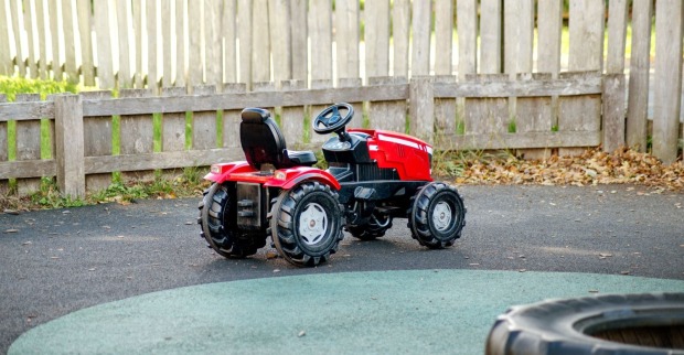 Ein roter Kinder-Trettraktor steht im Freien