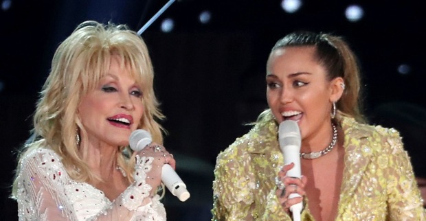 Dolly Parton und Miley Cyrus singen gemeinsam mit Mikrofonen auf einer Bühne.