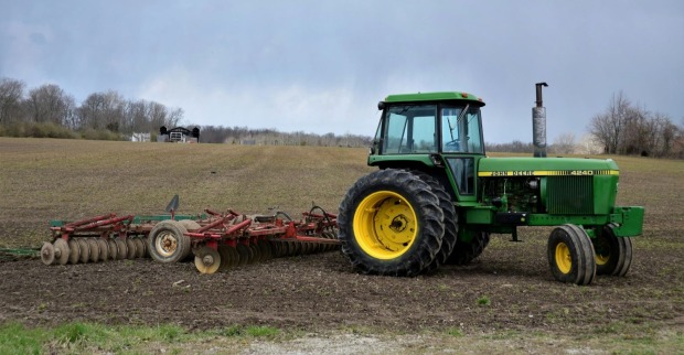 Grüner Traktor mit gelben Rädern und angehängtem Ackergerät auf einem Feld./ Ein 12-jähriger Bub ist bei einem Traktorunfall in Bünde verunglückt