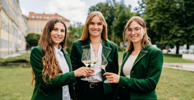 Drei Frauen in grünen Jacken stoßen mit Weingläsern an