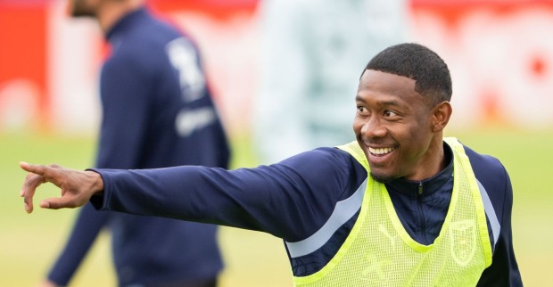 David Alaba lächelt beim Training und zeigt mit ausgestrecktem Arm zur Seite.