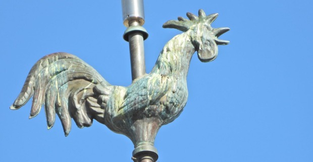 Ein traditioneller Wetterhahn auf einem Kirchturm vor spätsommerlichem blauen Himmel