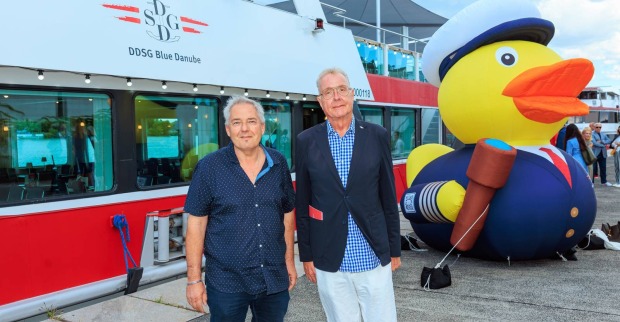 Zwei Männer in Casual-Kleidung vor einem Donauschiff und einer großen Gummiente